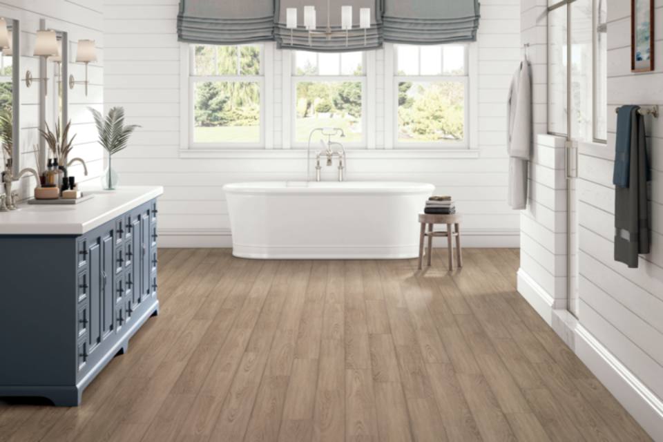 luxury viny plank flooring in bathroom with white tub and blue cabinets.